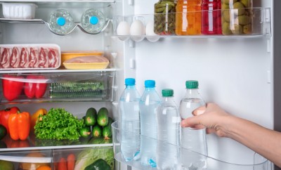 Young woman taking bottle of cool water from refrigerator
