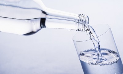 Pouring water from a glass bottle to a glass on a blue background. Close-up on pure drinking water