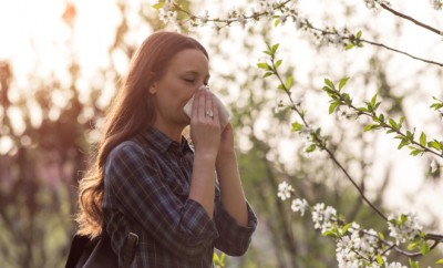 Young pretty girl blowing nose in front of blooming tree. Spring allergy concept