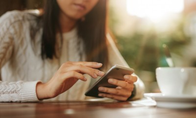 Young asian woman sitting at a table using mobile phone. Smart phone in hands of a female at outdoor cafe.