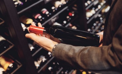 Bartender sommelier takes bottle of red wine from counter of restaurant drinks store.