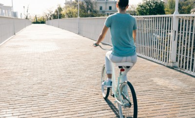 Slim girl in jeans and a T-shirt on a blue bike rides through the city on a sunny morning
