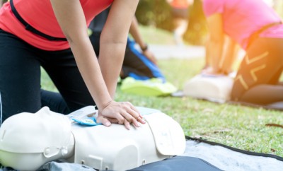 Asian female or runner woman training CPR demonstrating class in park by put hands and interlock finger over CPR doll give chest compression. First aid training for heart attack people or lifesaver.