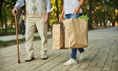 Cropped head portrait of old male with adult female walking through the city park with foodstuff in packages