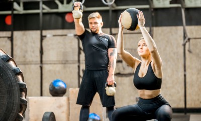 Young athletic couple in black sports wear training with weights and ball in the crossfit gym