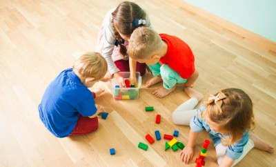 Lovely children at day care centre sitting on a floor putting colorful wooden blocks into plastic box. Kids collecting multicolor blocks in strict order into plastic box at Montessori centre.