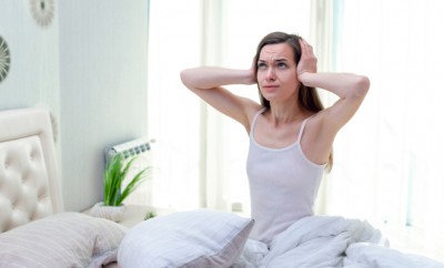 Young woman suffering and disturbed by noisy neighbors and covering her ears with hands while trying to sleep in bed at home in early morning