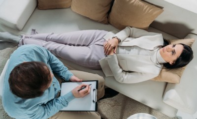 overhead view of psychotherapist writing on clipboard and upset young patient lying on couch