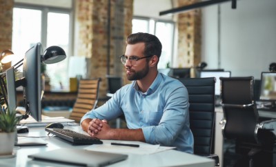 I am so busy today. Young andsuccessfulbearded man in eyeglasses and formal wear looking at computer monitor during his working day in modern office. Workplace. Business concept