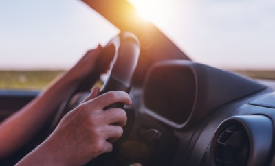 Driving car through countryside, female hands on steering wheel, close up with selective focus