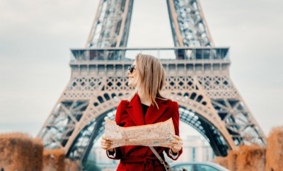 Style redhead girl in red coat and bag with map in parisian park in autumn season time. Eiffel tower on background
