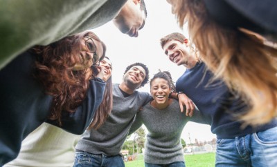 Multiracial group of friends embraced in a circle, strong concept about teamwork and cooperation, also refers to immigration and friendship.