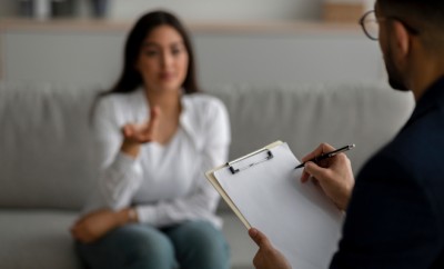 Stressed arab woman consulting psychologist at medical office, selective focus. Psychiatrist helping desperate middle eastern lady with nervous breakdown, taking notes during session