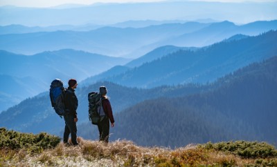 The couple with backpacks standing on the mountain with a beautiful view