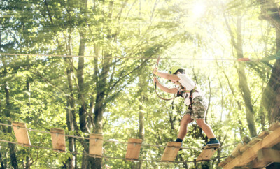 Happy little boy passing the cable route high among trees, climb