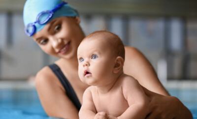 Adorable little baby with coach in swimming pool, closeup