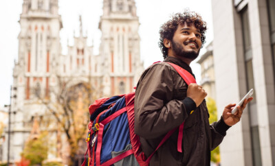 Positive indian traveler with backpack using smartphone in city