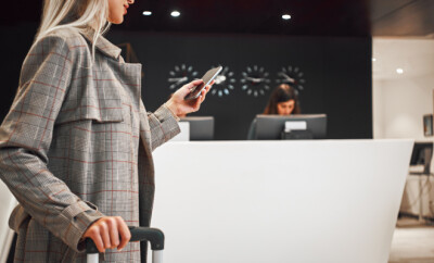 Hotel personal waiting for a client. Full length portrait of a smiling successful businesswoman pulling suitcase and talking on the phone in the hotel. Close-up of blonde woman with smartphone